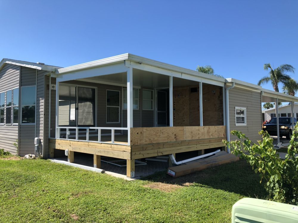 House with a partially built screened porch. Deck, gray siding, white trim, and blue sky.