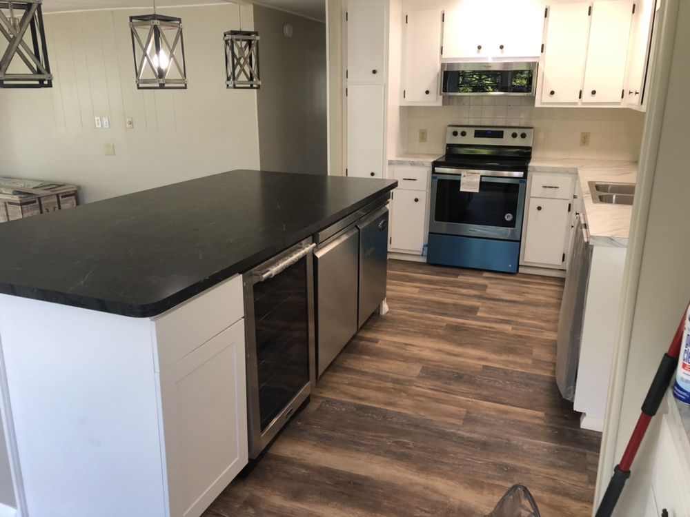 Kitchen with black island countertop, stainless steel appliances, white cabinets, and wood-look flooring.