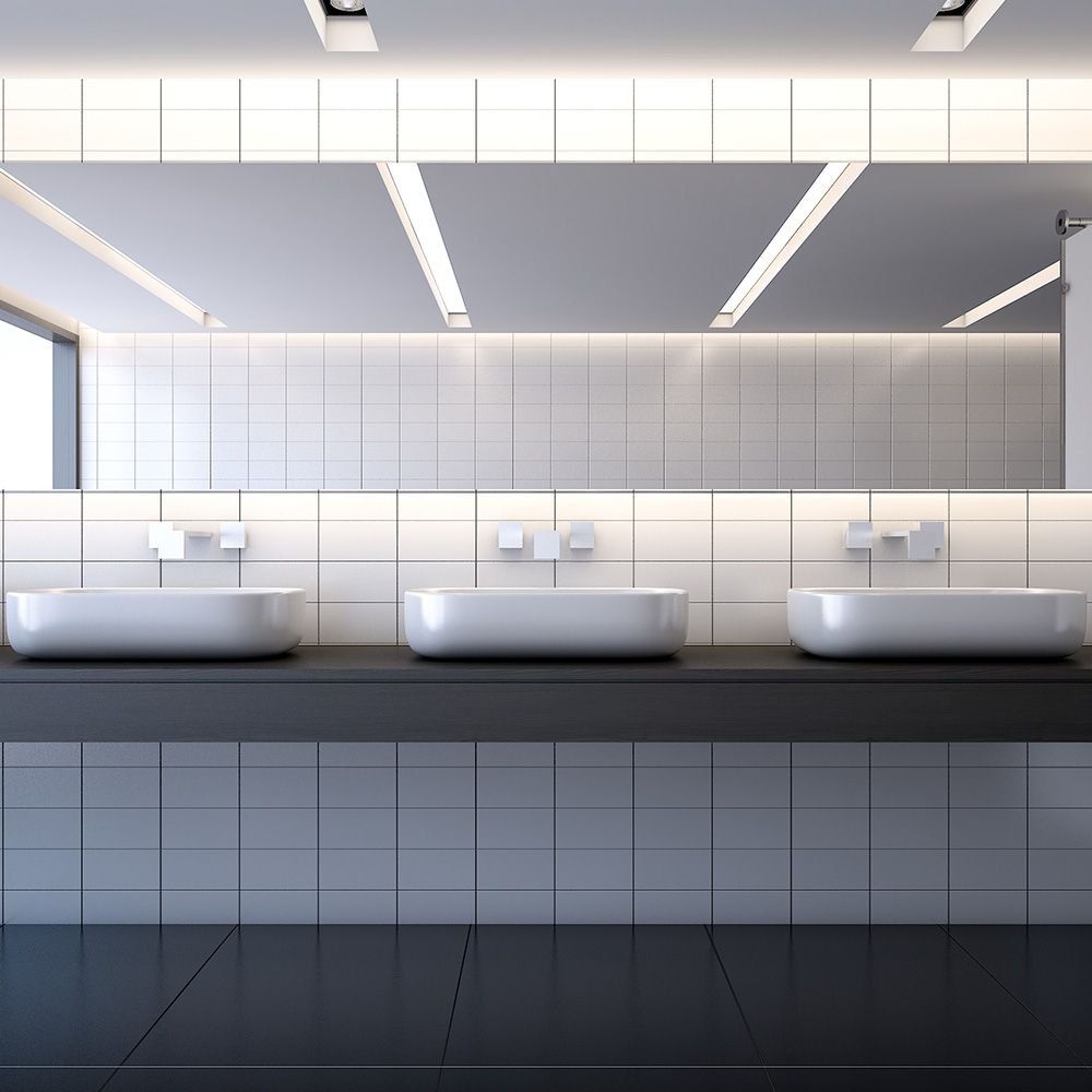 Modern public restroom with three white sinks, large mirror, and white tiled walls and floor.