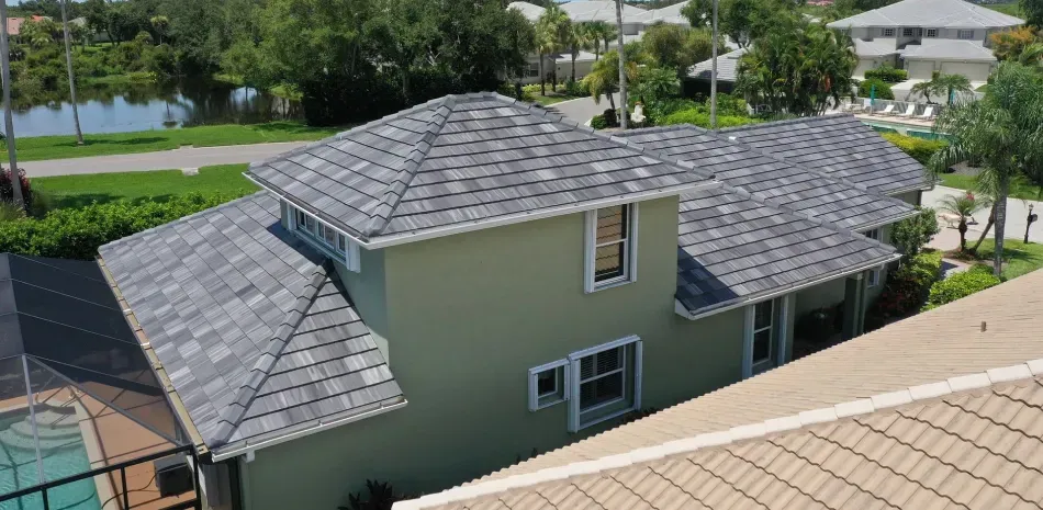 An aerial view of a two-story house with a gray roof, painted green, near a body of water.