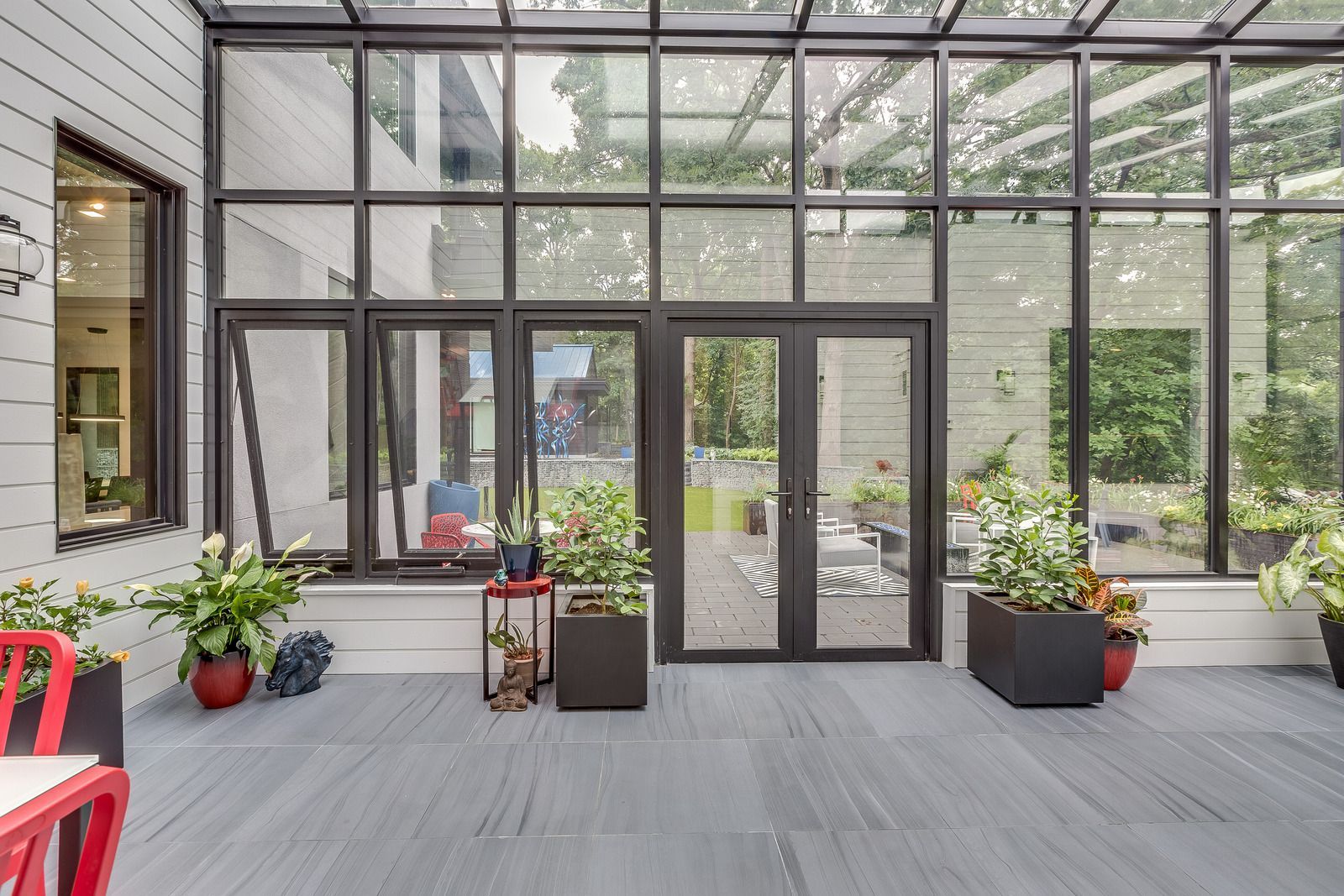 Sunroom with large windows, gray patio, potted plants, and red chair.
