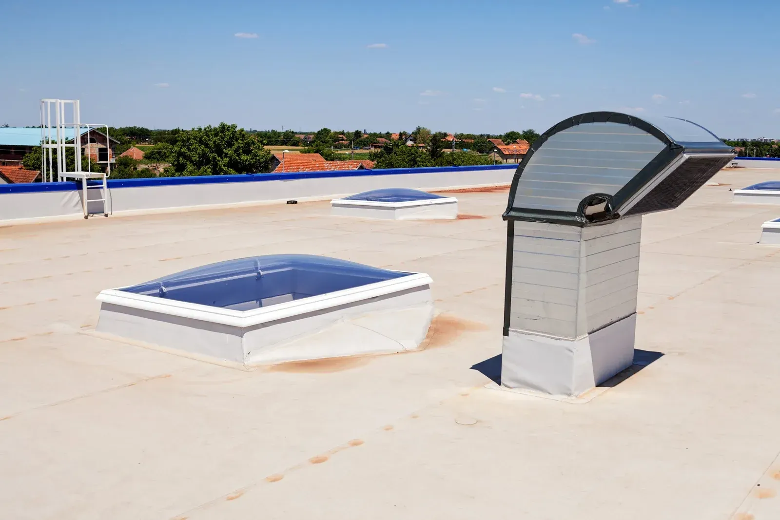 Flat commercial roof with skylights and ventilation unit under a blue sky.