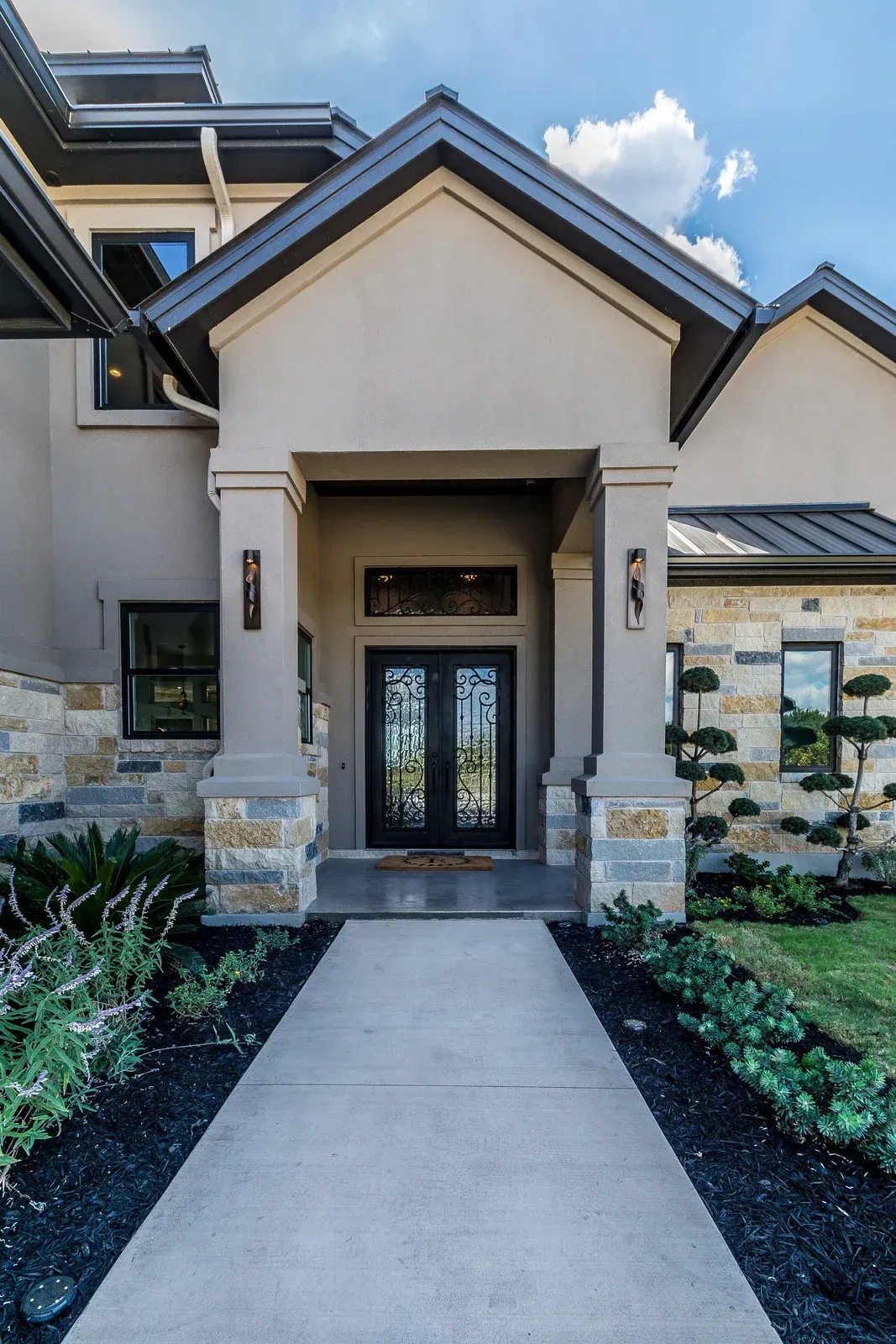 House exterior with covered entrance, stone and tan facade, double black doors, concrete path.