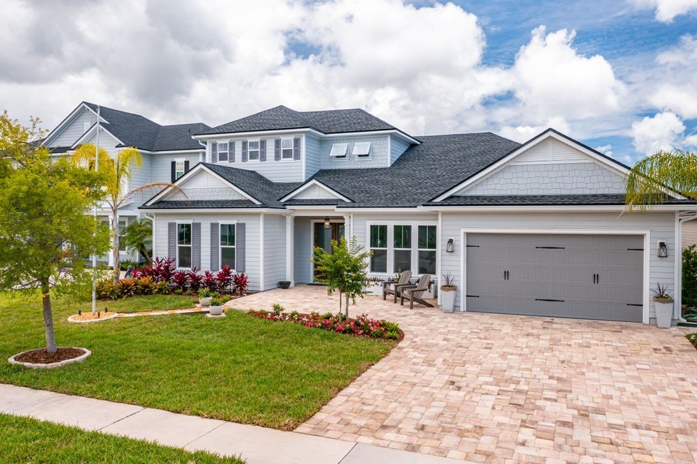 A large white house with a gray garage door and a brick driveway.