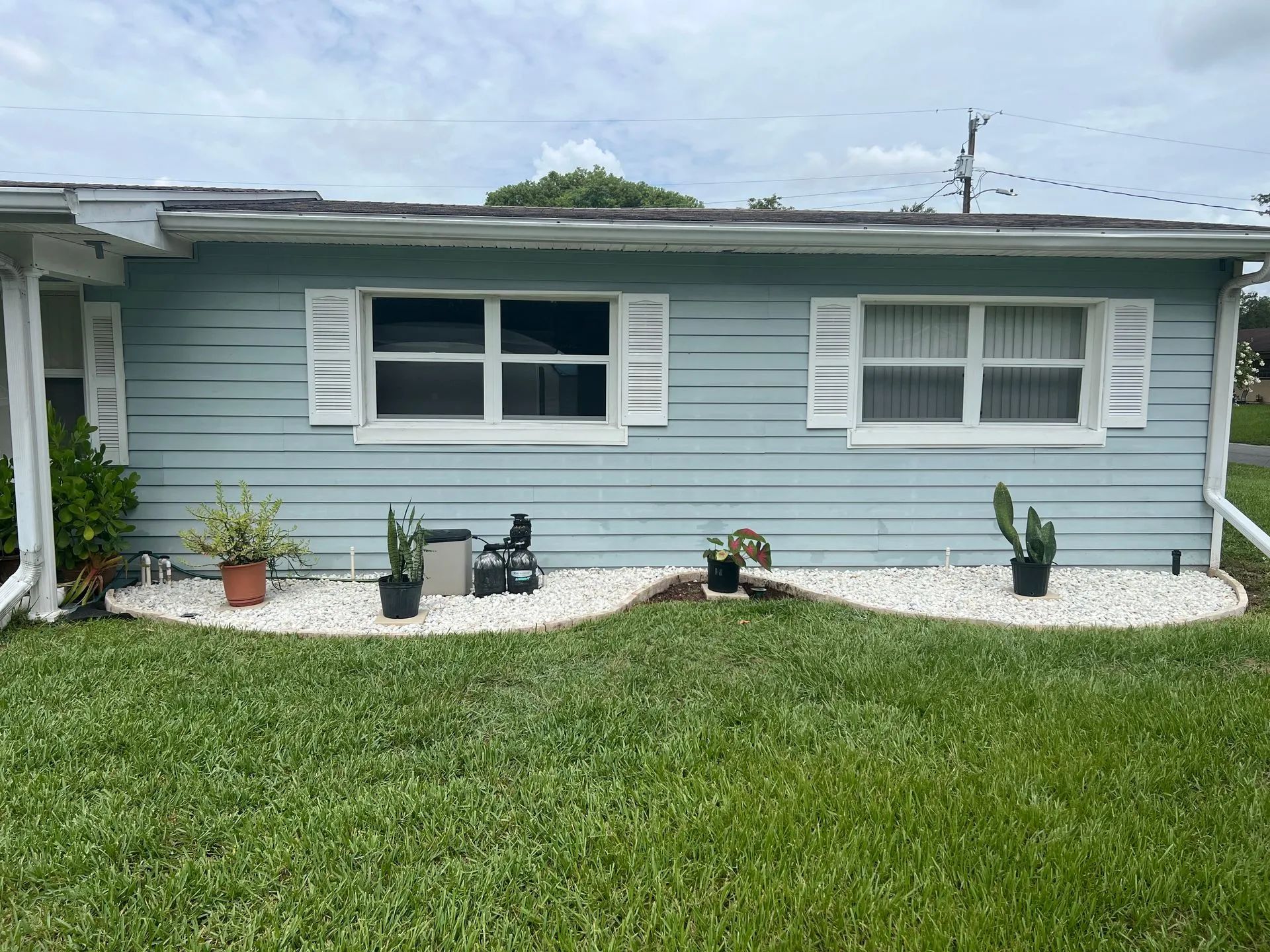 A blue house with white shutters and potted plants in front of it.
