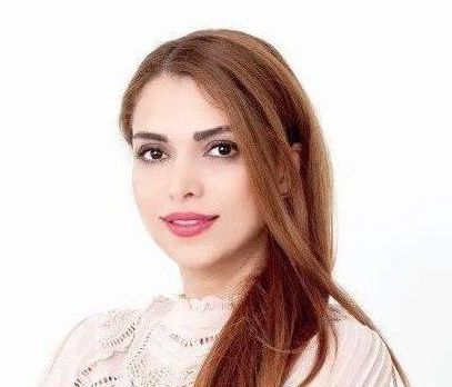 Woman with light brown hair and makeup, smiling, wearing a light colored top against a white background.