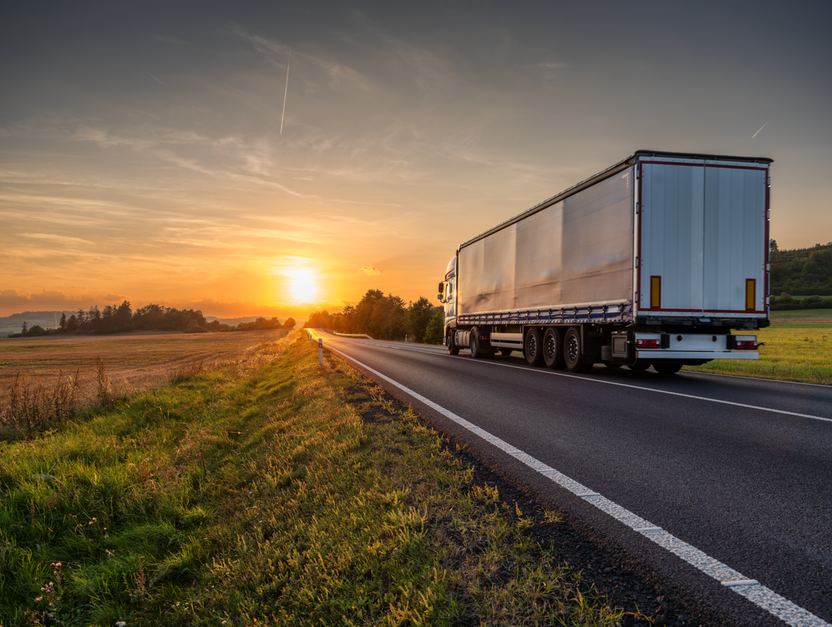 Semi-truck driving on a road at sunset.