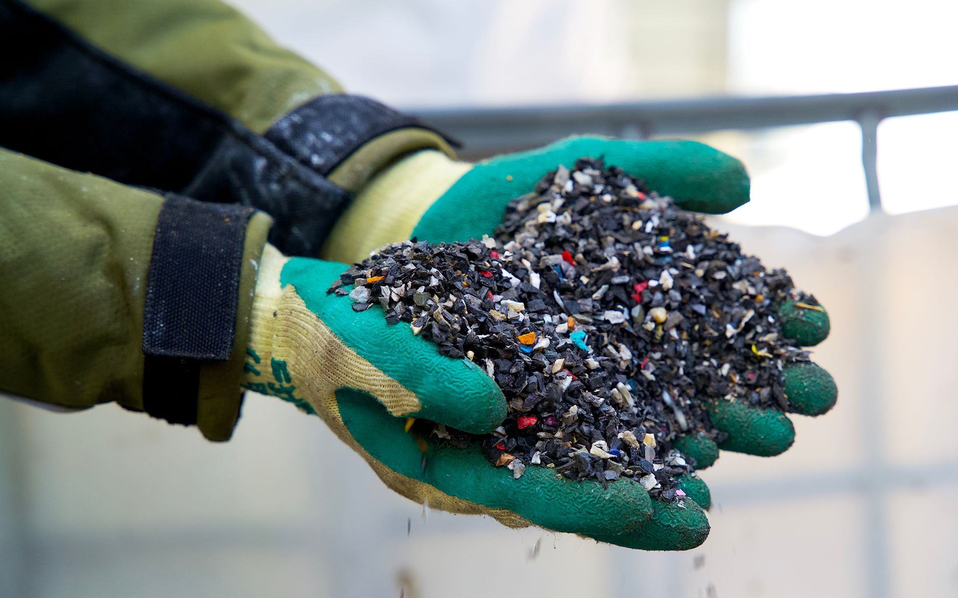 Hands in green gloves holding a pile of small, recycled plastic pieces, likely for reuse.