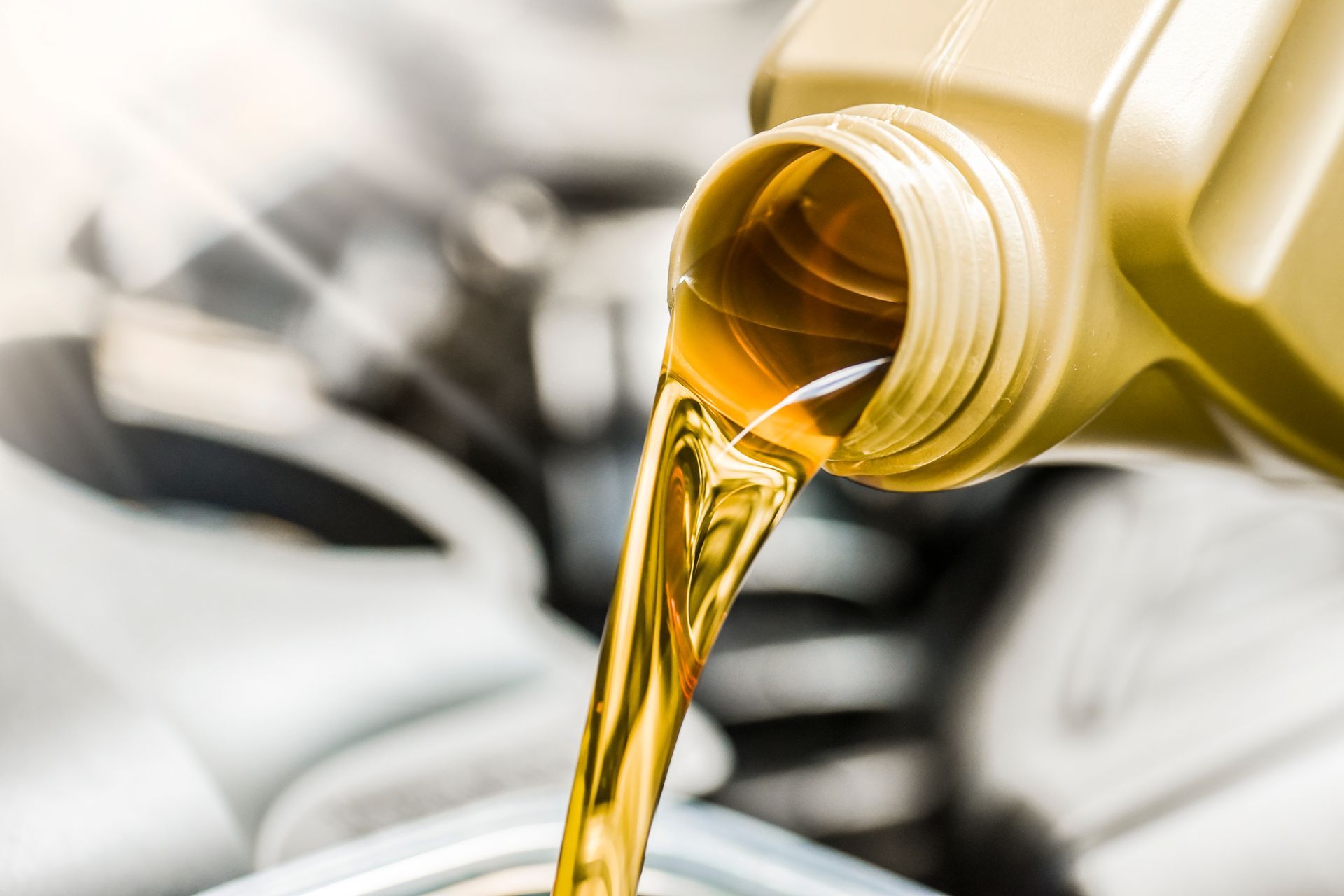 Yellow motor oil pouring from a container into a car engine.