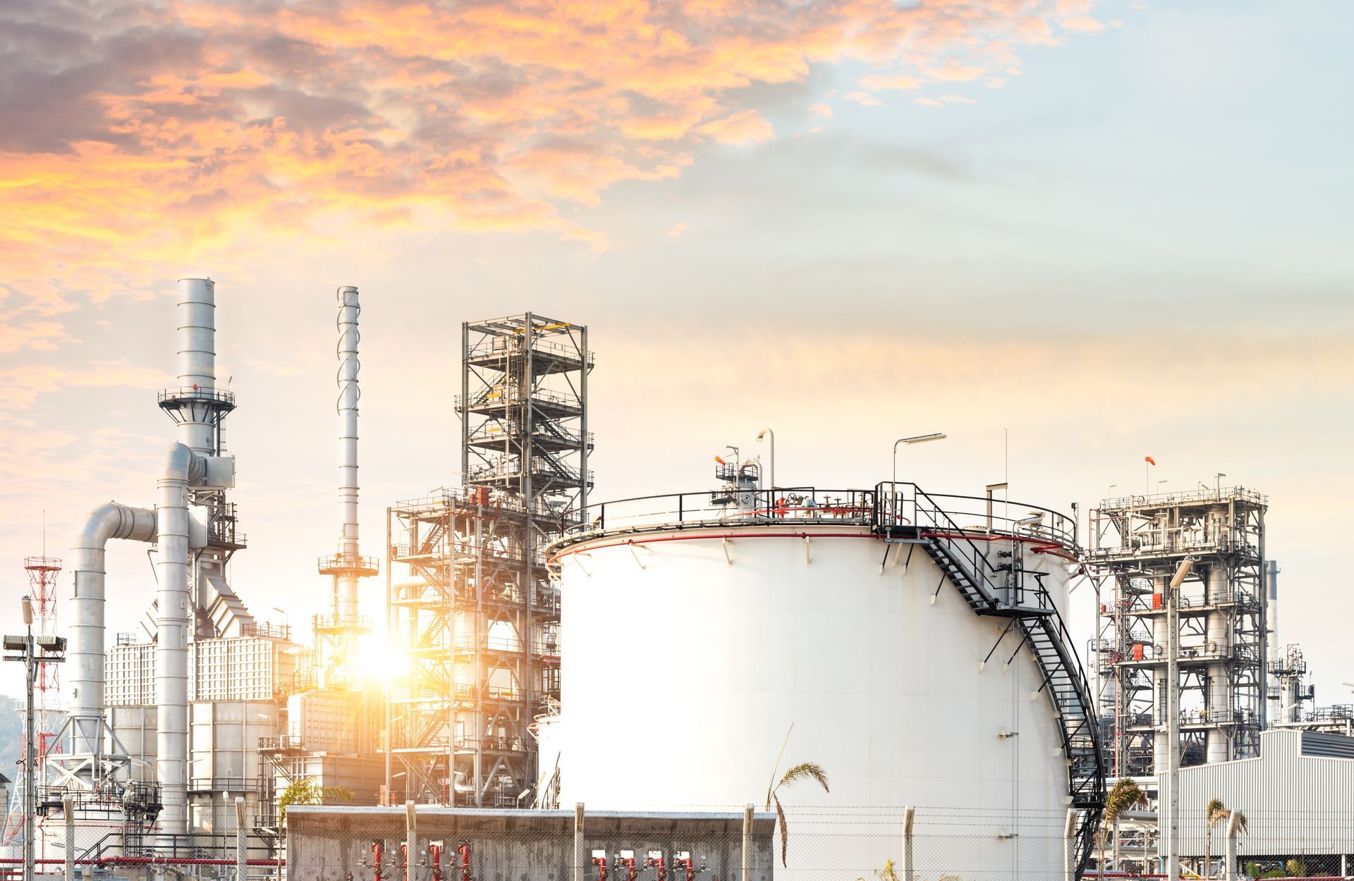 Oil refinery against a sunset sky. Large white storage tank and industrial structures.