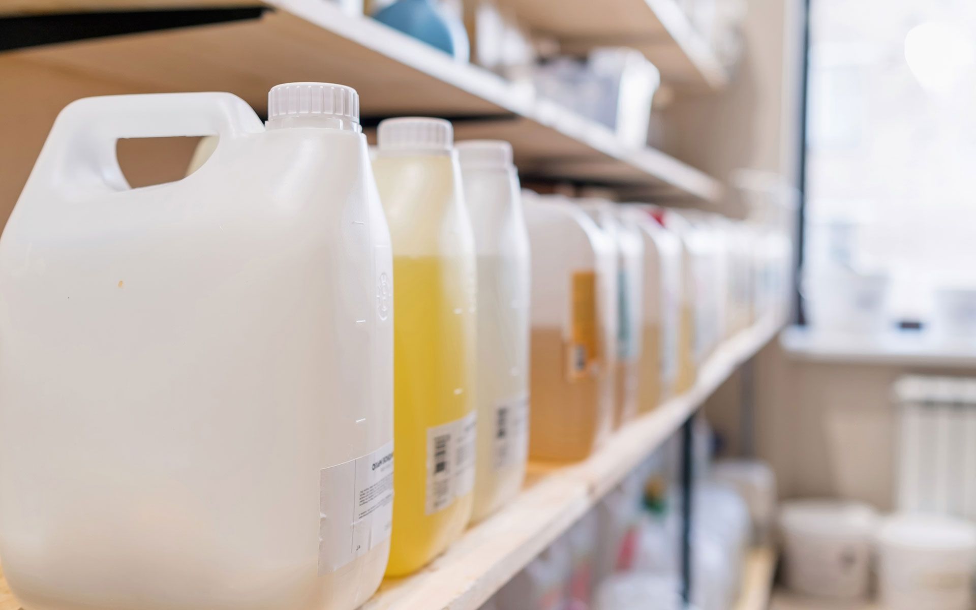 White plastic jugs with colorful liquids on a wooden shelf in a shop.