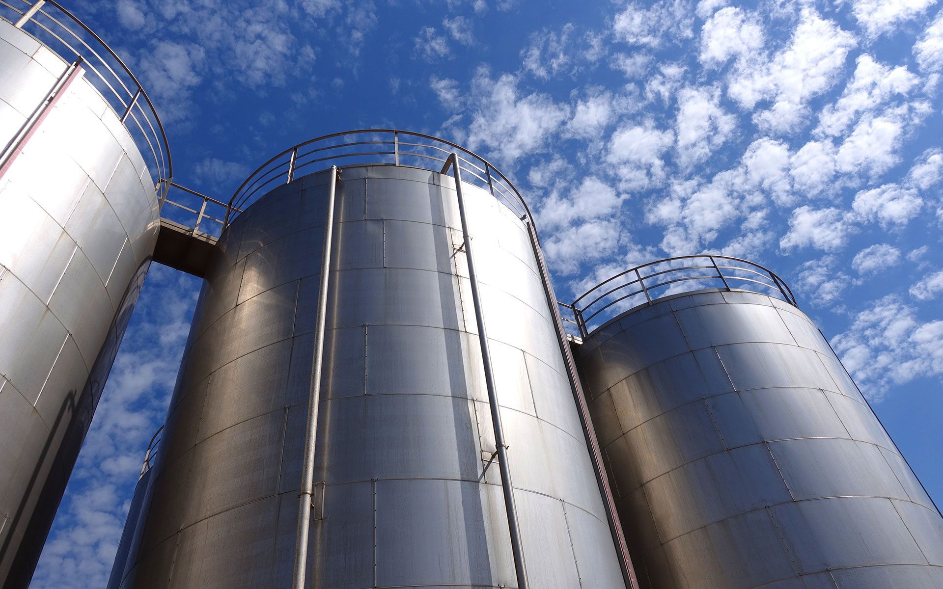 Large silver industrial storage tanks against a blue sky with clouds.