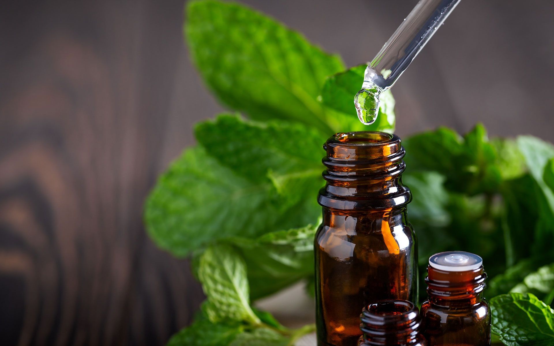 Dropper dispensing liquid into a small brown bottle with mint leaves in the background.