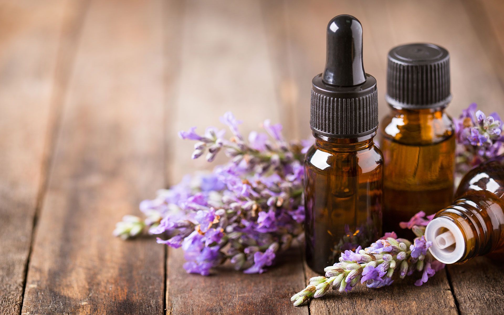 Bottles of essential oil with lavender sprigs on a rustic wooden surface.