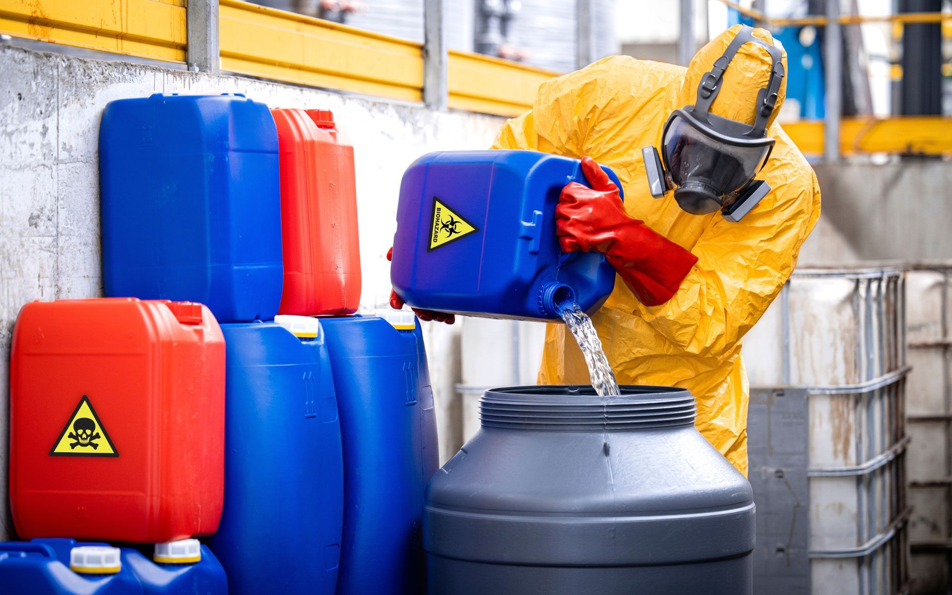 Person in hazmat suit pouring liquid from container with biohazard symbol into a drum.