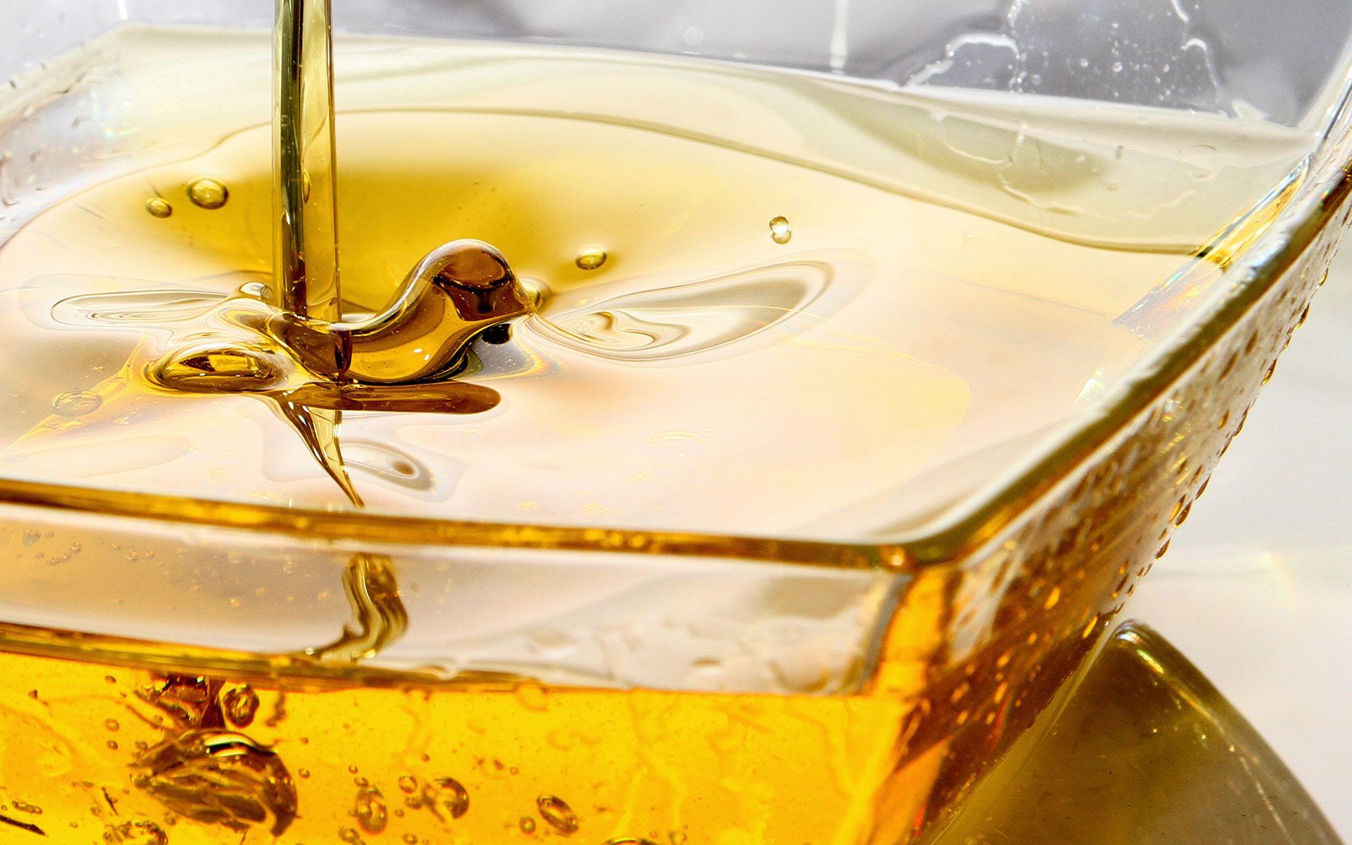 Honey pouring from above into a clear glass dish, creating ripples, amber hues.