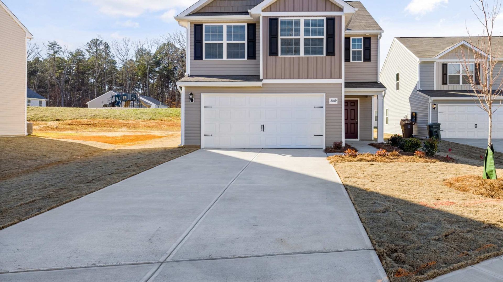 Suburban two-story house with a white garage, concrete driveway, and dry lawn under clear daylight