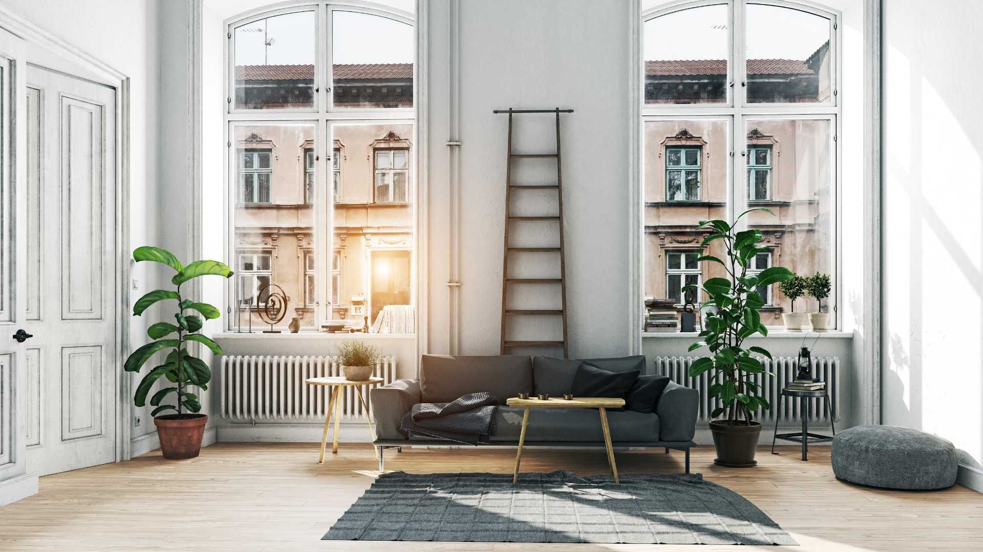 Sunlit modern living room with sofa, plants, ladder, and large windows overlooking a city street