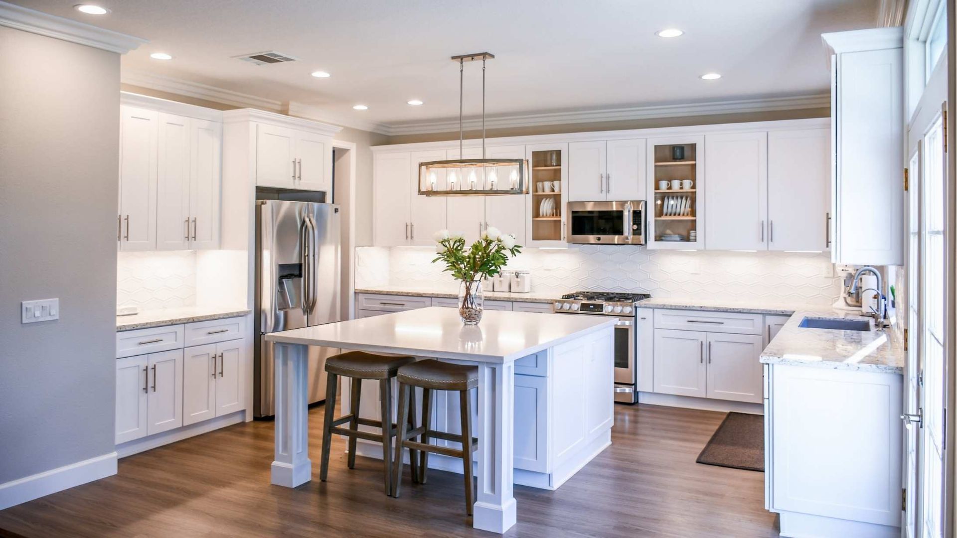 Bright modern white kitchen with island, wood floors, stainless fridge, and pendant lights