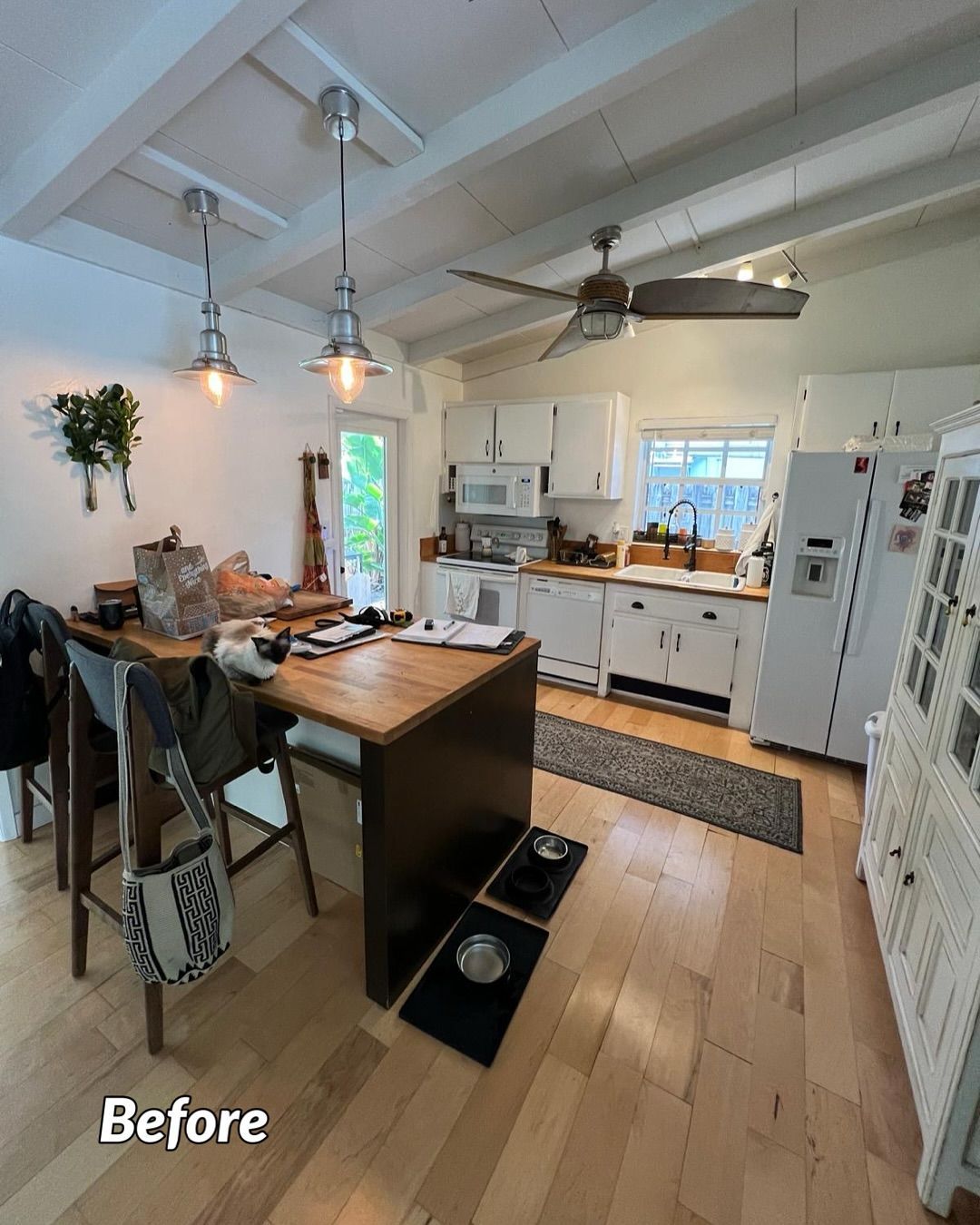 Kitchen with wood floors, white cabinets, and a dark wood island. A dining table with chairs is on the left.