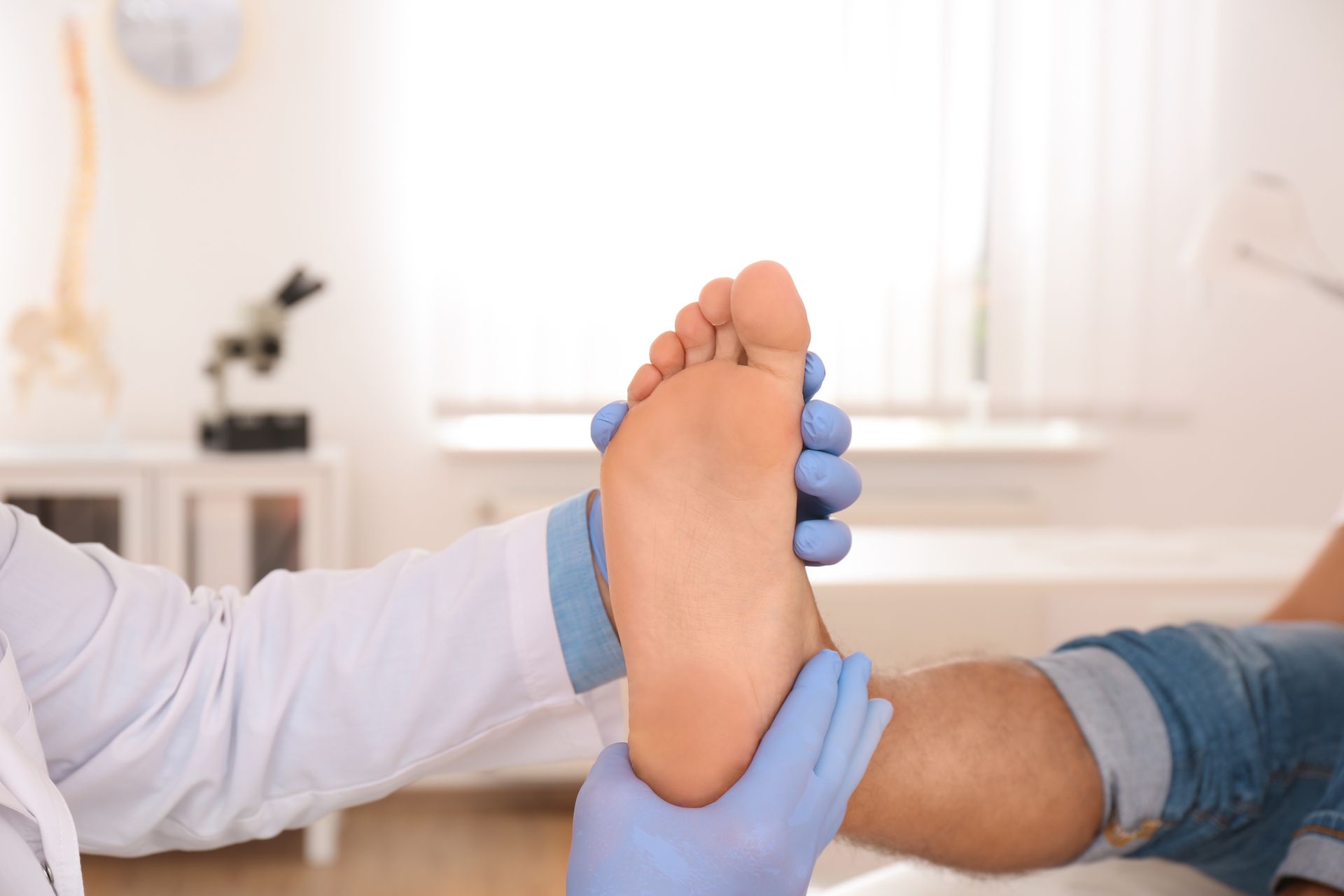 Doctor examining a patient's foot in a medical setting, wearing gloves and a lab coat.