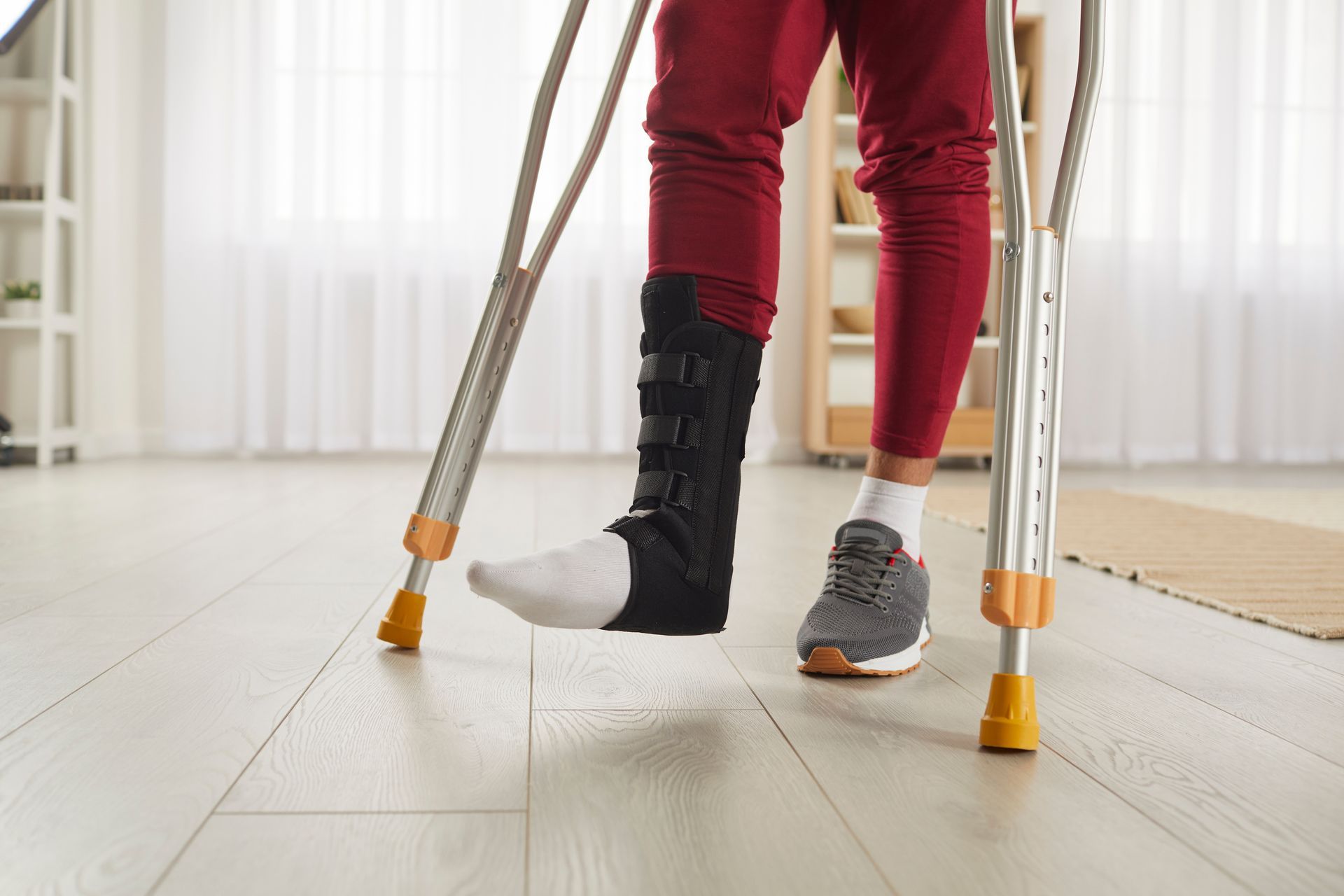 Person with a leg brace and crutches indoors, light-colored wood floor.