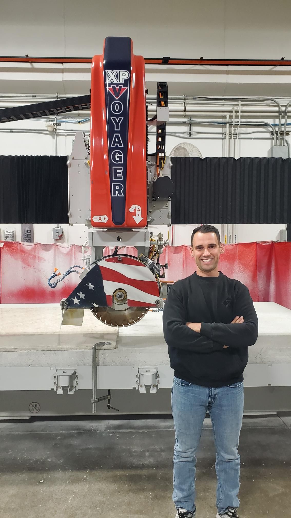 Man stands in front of a large stone-cutting machine; Puerto Rican flag is visible on the blade.