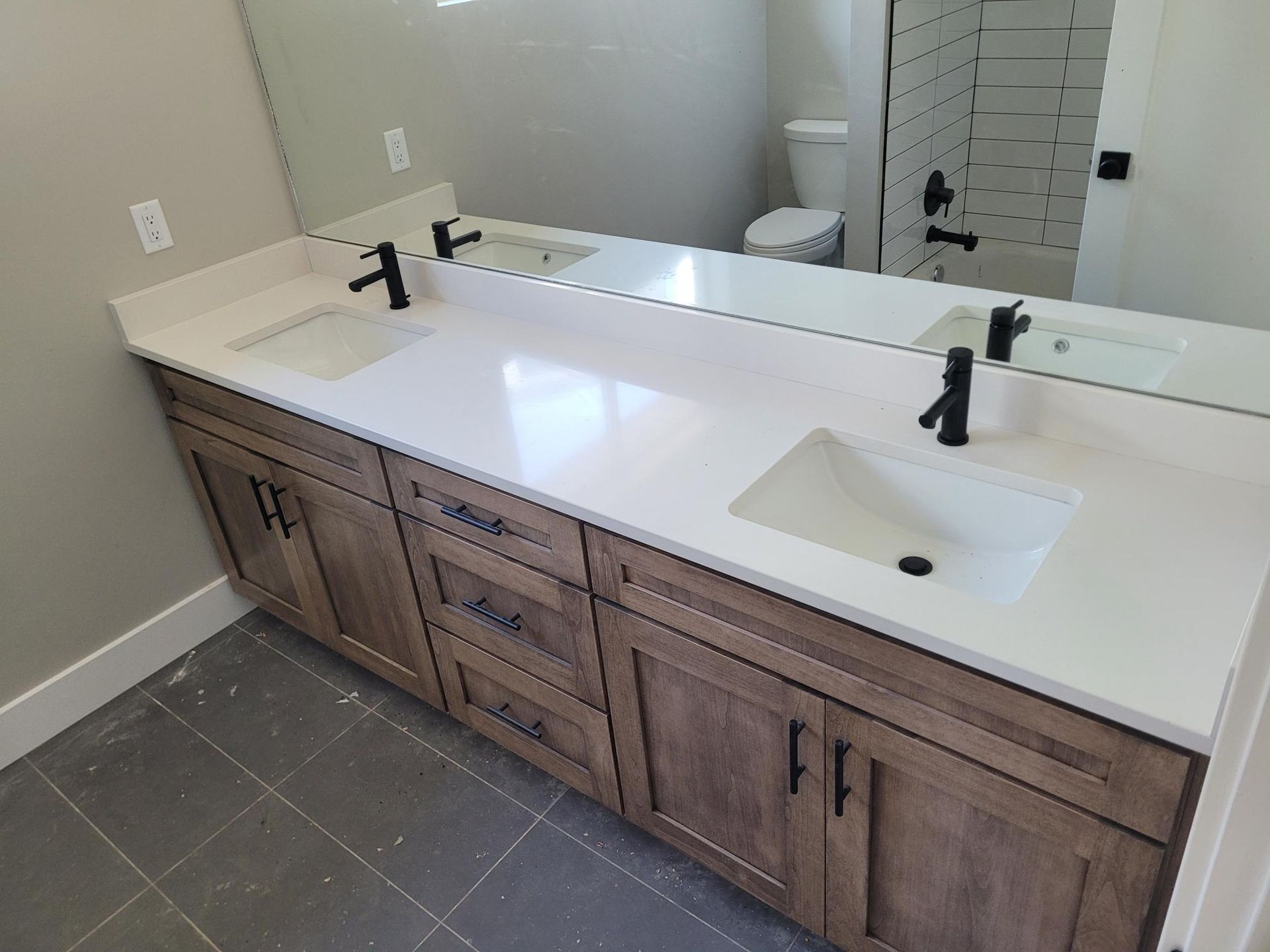 Bathroom vanity with light wood cabinets, white countertop, black faucets, and rectangular sinks.