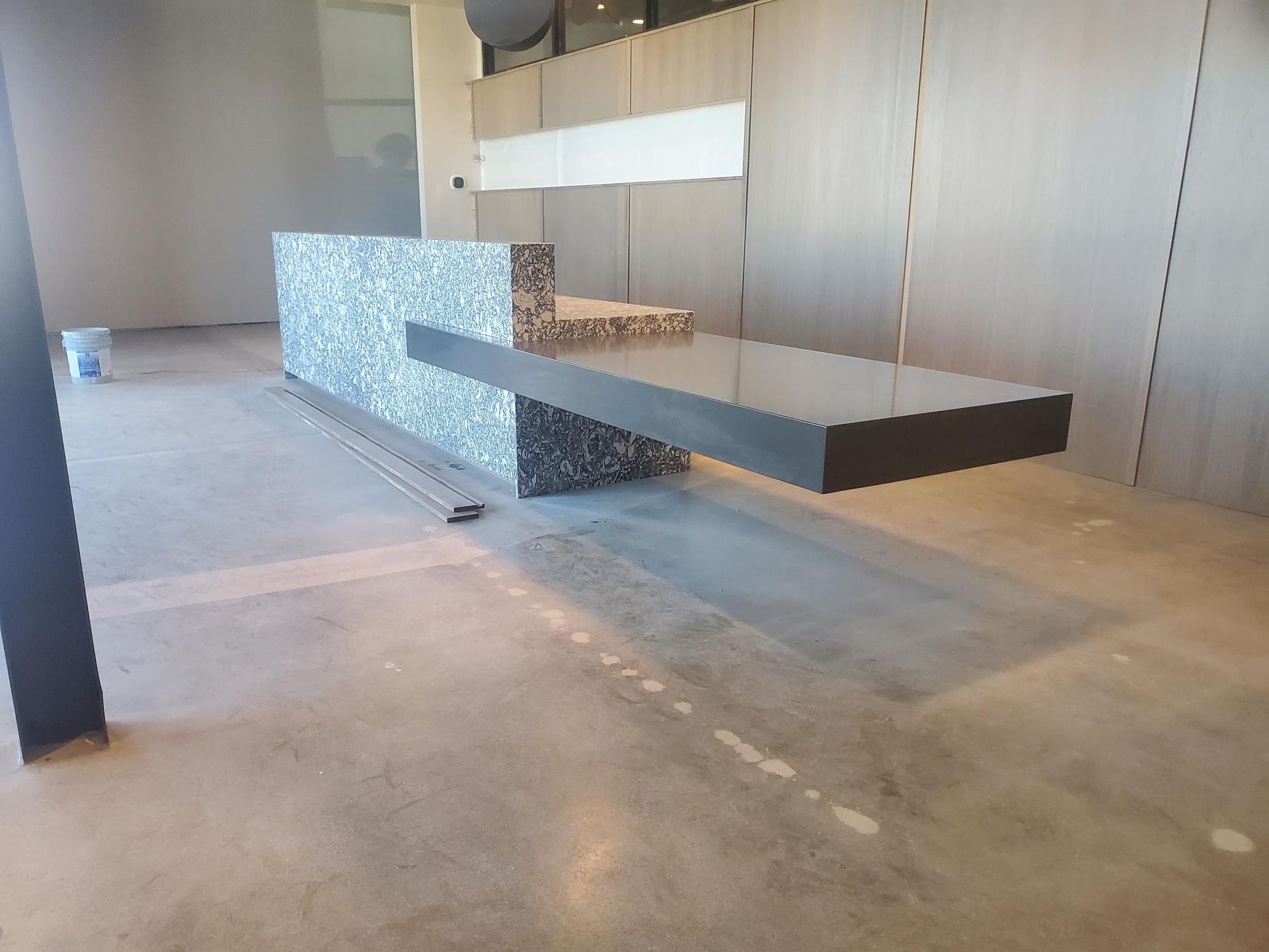 Modern, geometric reception desk; gray and textured surfaces, floating dark countertop. Concrete floor.