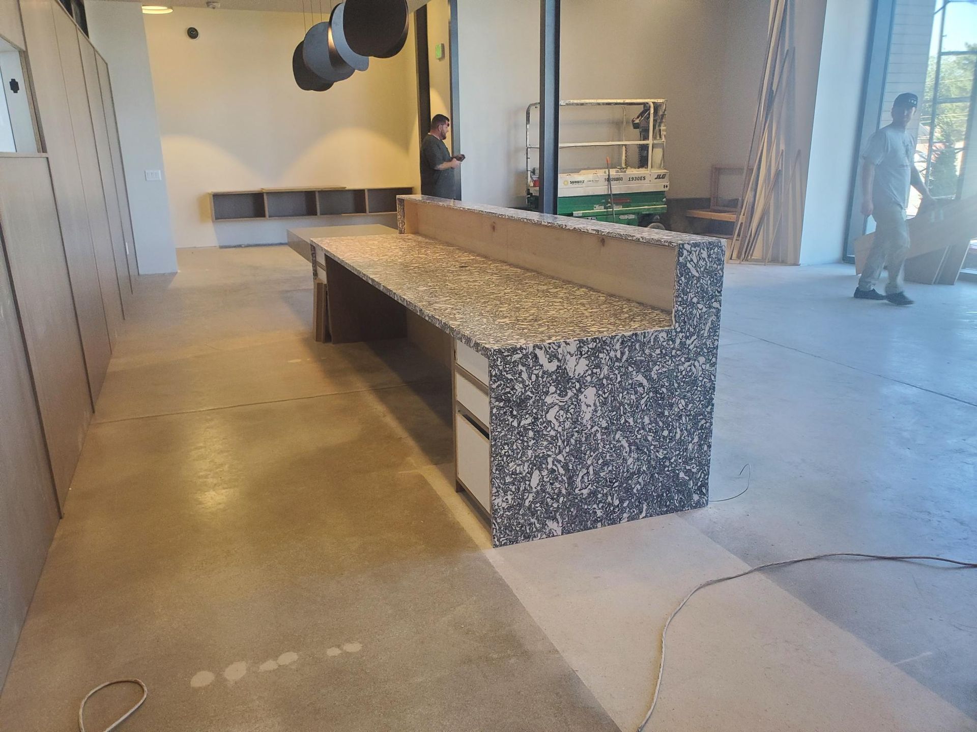 A counter with a textured surface in a room under construction, with workers visible.