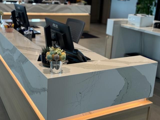 Reception desk with a marble-like countertop. A vase with flowers sits on the corner.