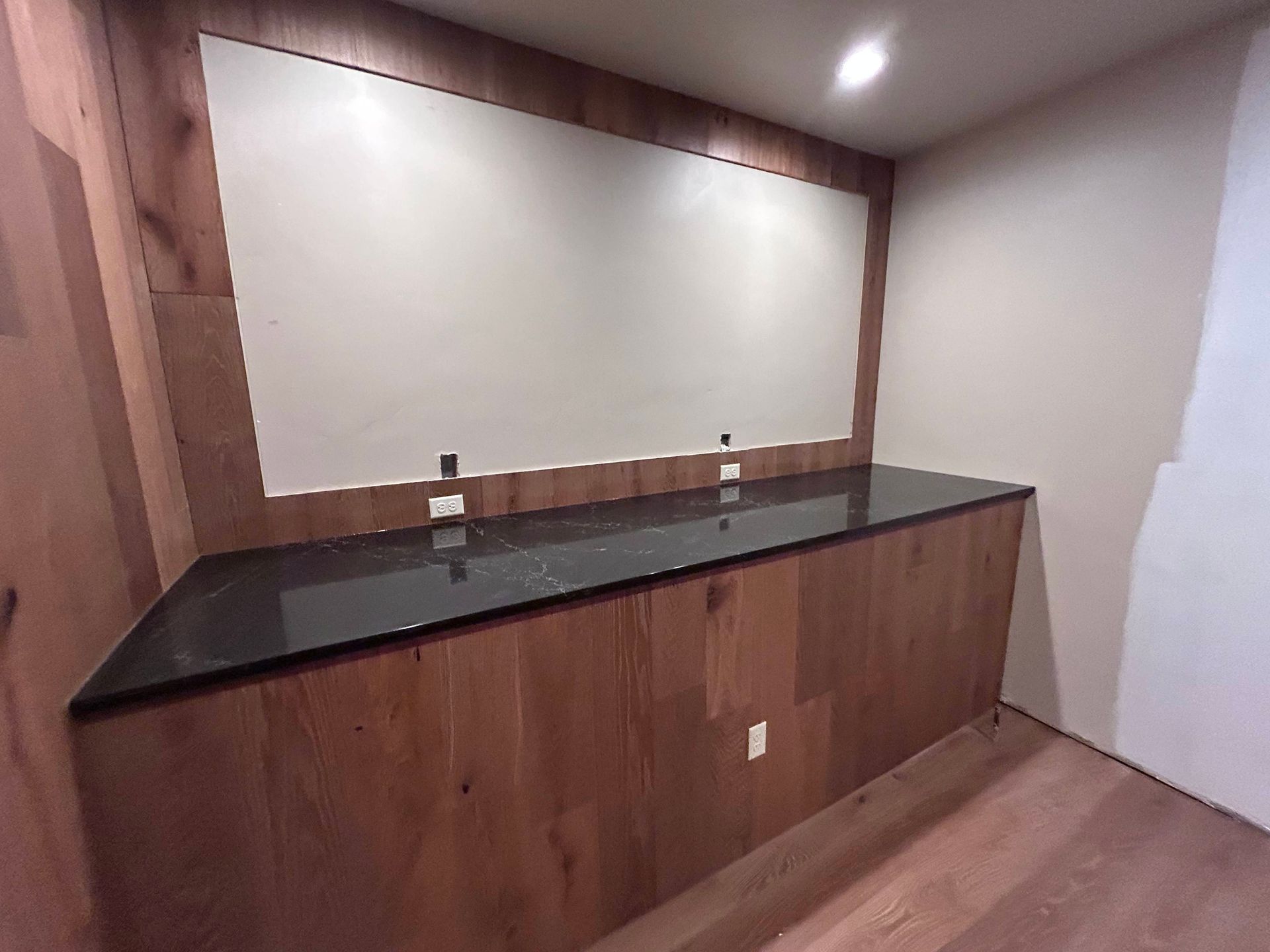A built-in desk with a black countertop and a whiteboard set into wood paneling.