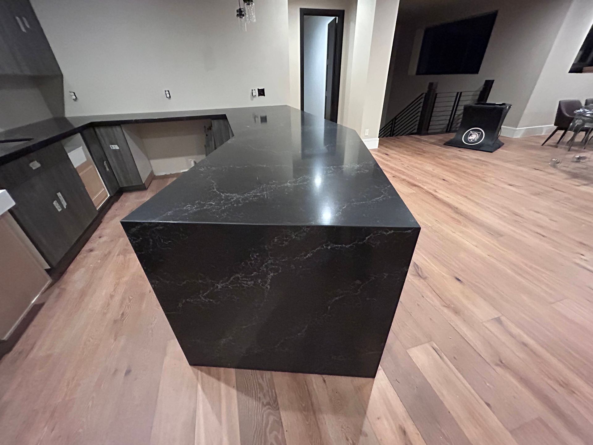 Dark kitchen island and countertop with light wood flooring. Cabinets and a television are visible.