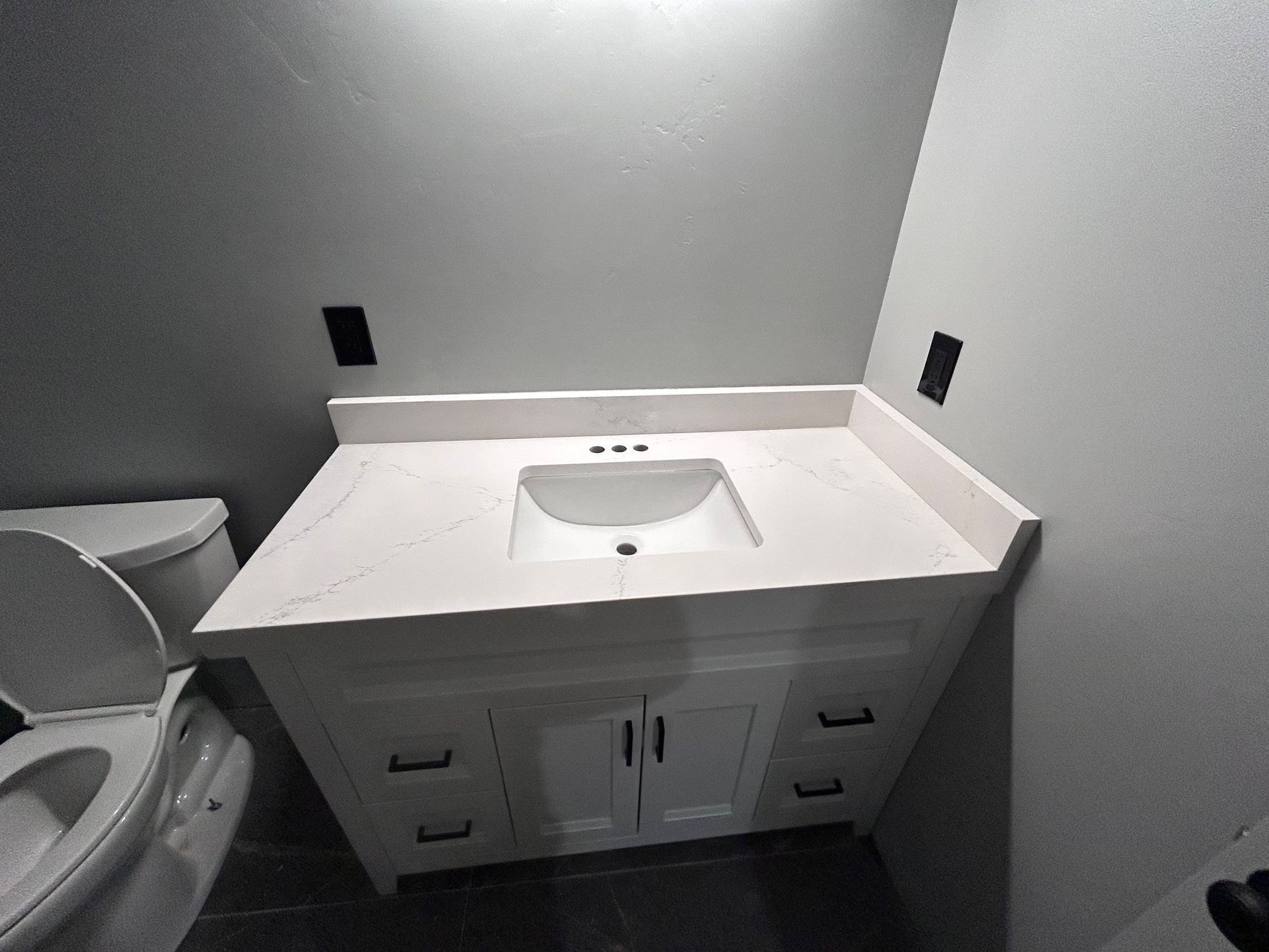Bathroom vanity with a granite countertop, sink, faucet, and decorative backsplash.