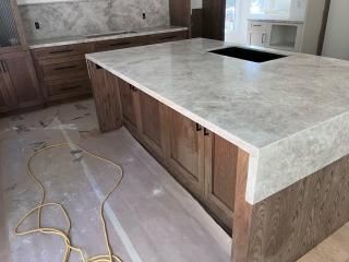 Kitchen island with gray marble countertop and wooden cabinets; wires on floor.