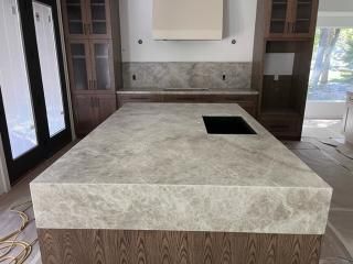 Modern kitchen island with gray countertop, wooden cabinets, and cooktop.