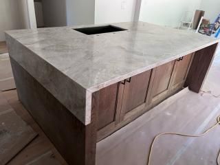 Kitchen island with a marble countertop and wooden cabinets. A sink is cut into the countertop.
