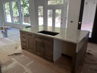 Kitchen island with light countertop and dark wood cabinets, sink, and open space.