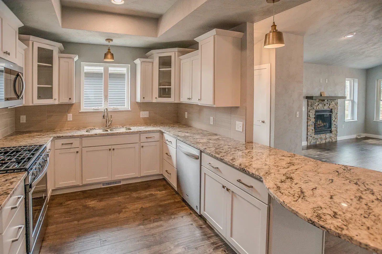 White kitchen with granite countertops, stainless steel appliances, and adjacent living room with fireplace.