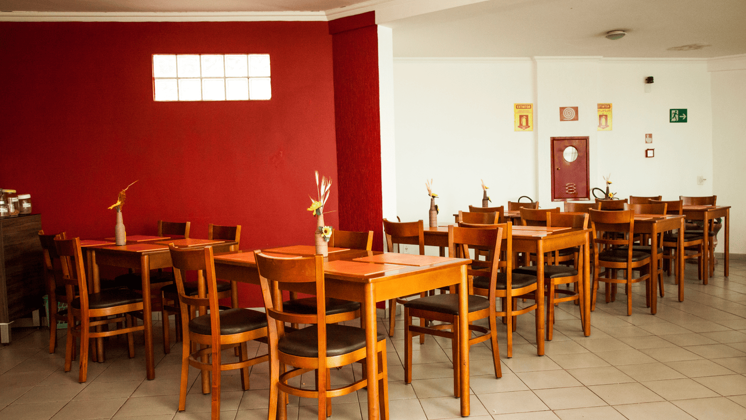 Uma sala de jantar com mesas e cadeiras e uma parede vermelha.