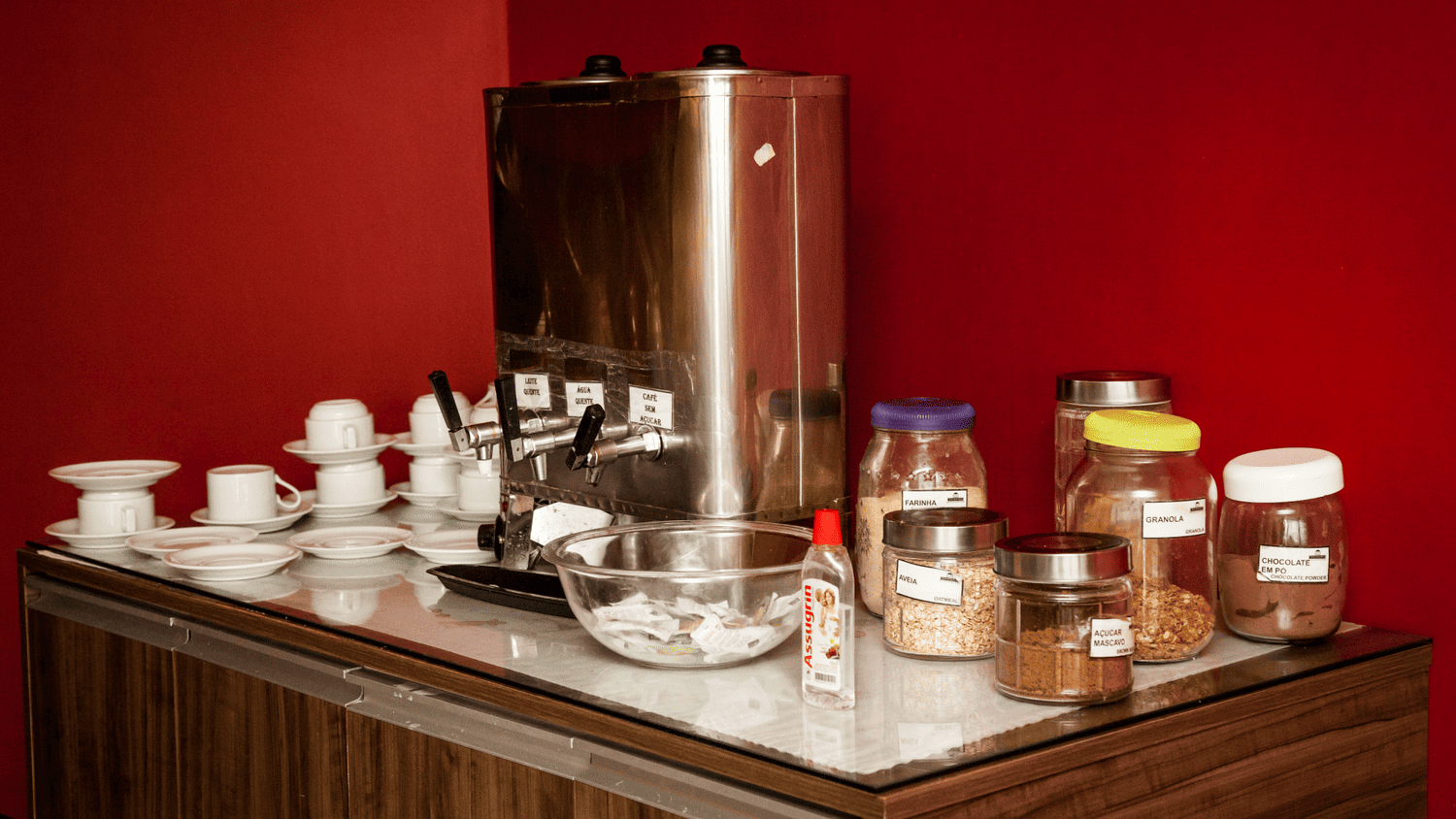 Uma mesa com uma cafeteira, xícaras e potes de comida.