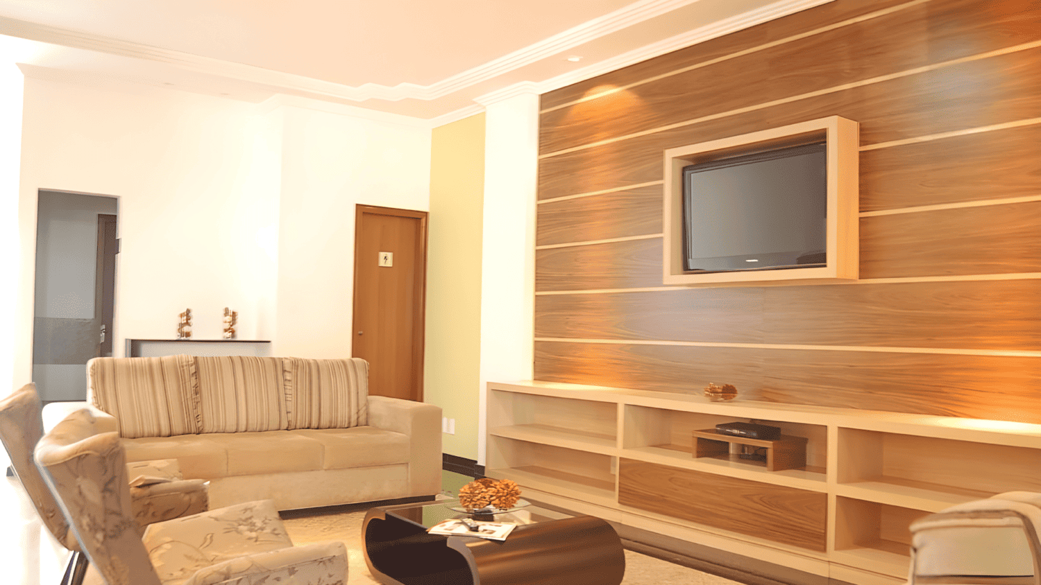 Uma sala de estar com um sofá, cadeiras e uma TV de tela plana.