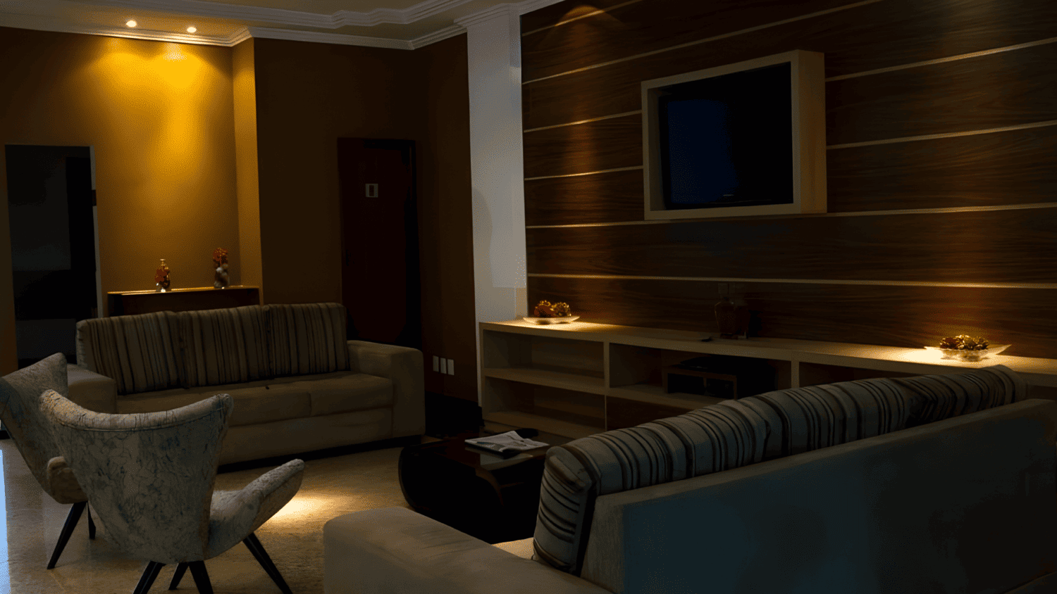 Uma sala de estar com sofá, cadeiras, mesa e televisão.