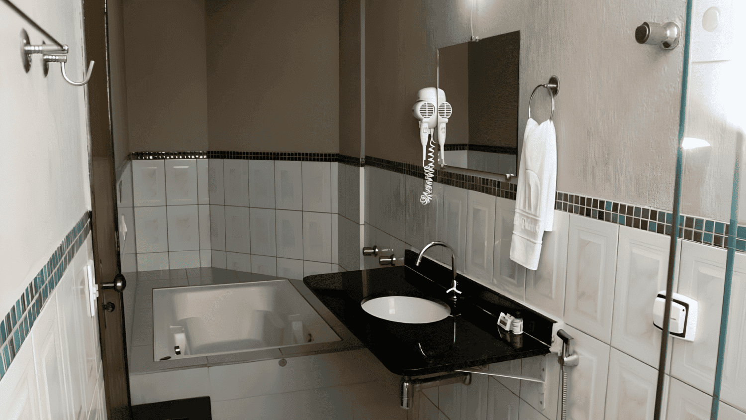 Um banheiro com banheira, pia, espelho e toalheiro.