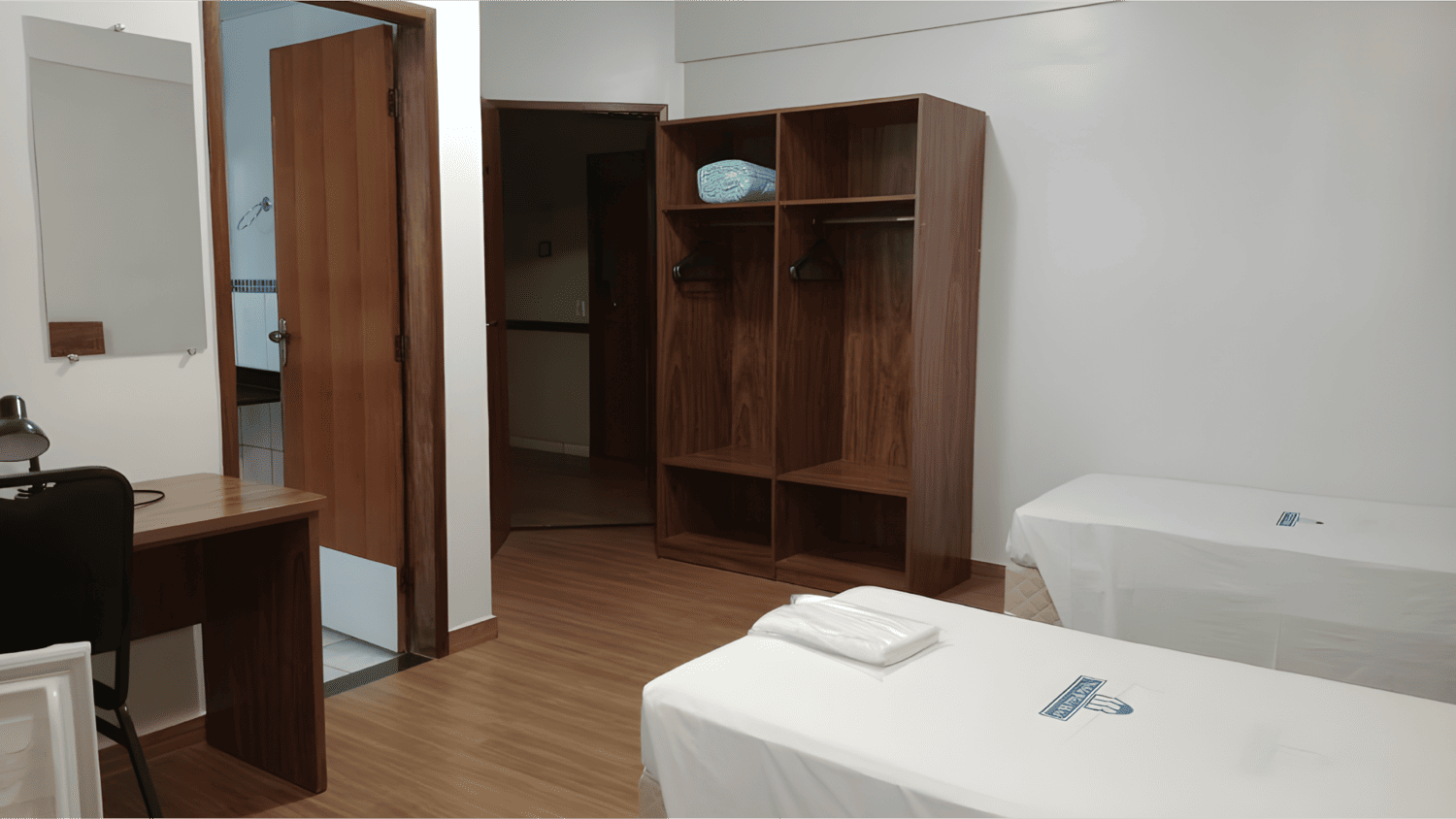 Um quarto com duas camas, uma escrivaninha, um espelho e um armário.