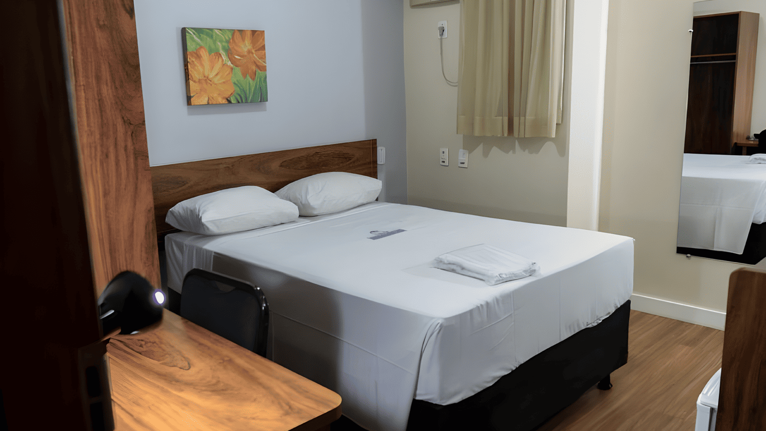 Um quarto de hotel com uma cama, escrivaninha, cadeira e espelho.