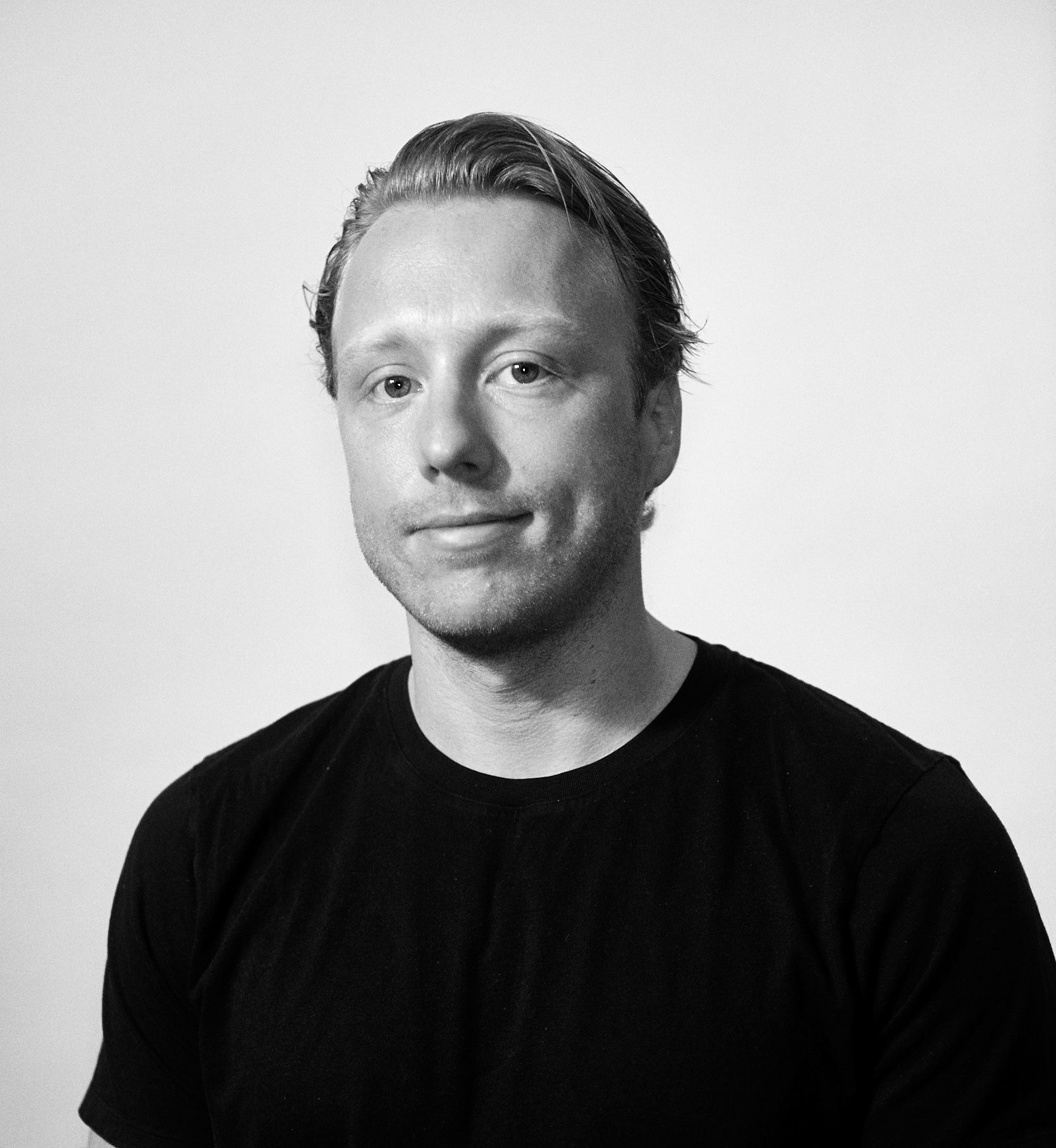 A man in a black shirt is smiling in a black and white photo.