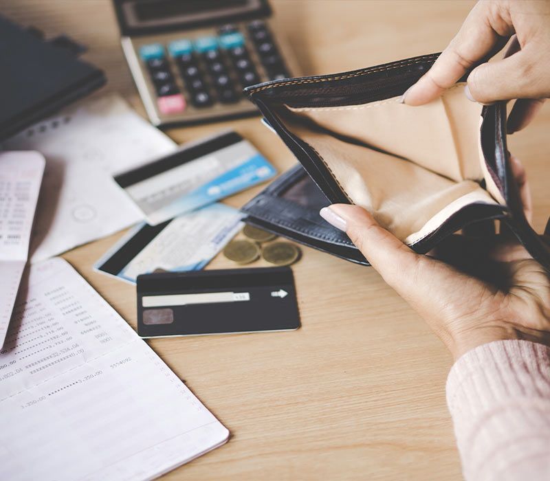 Empty wallet held open with bills, credit cards, coins, and calculator on a table.