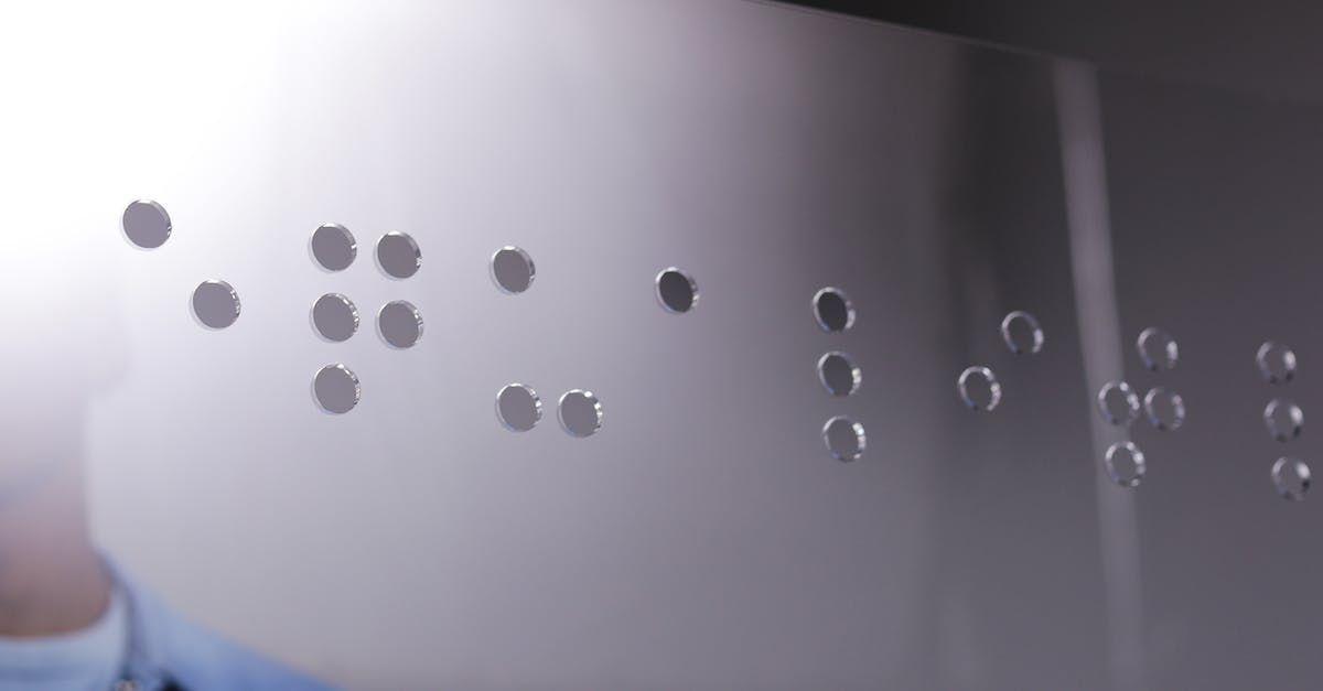 Braille dots on a reflective surface, possibly glass, with a person's arm in the corner.
