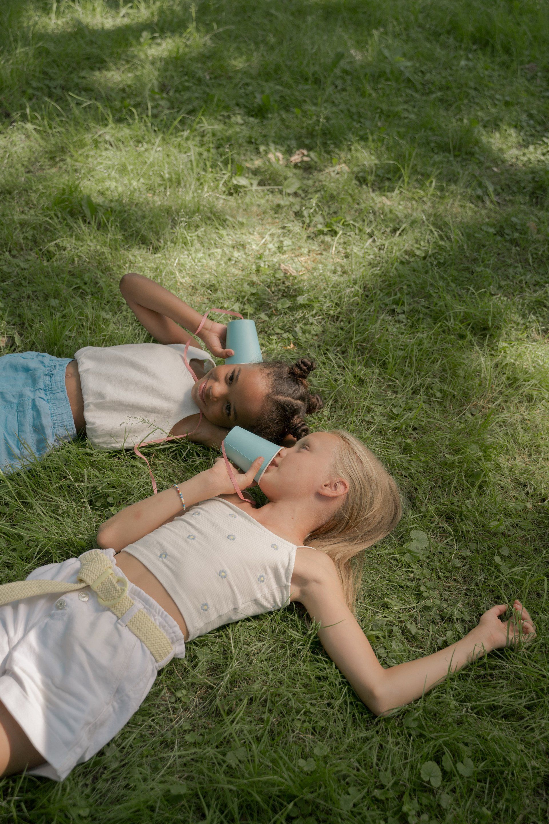 Two people lying in grass, using cups as phones.